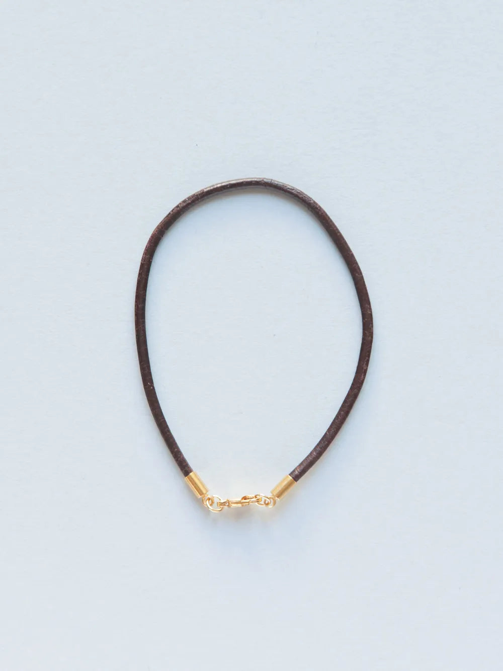Armband aus schmaler dunkelbrauner Lederkordel mit goldenem Verschluss auf weissem Hintergrund