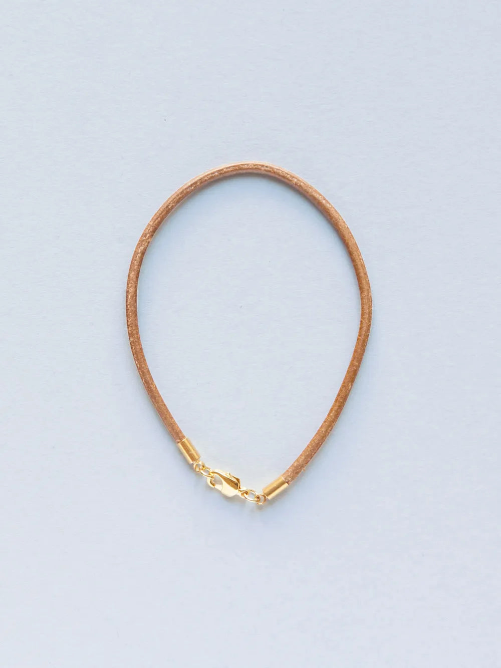 Armband aus schmaler natur Lederkordel mit goldenem Verschluss auf weissem Hintergrund