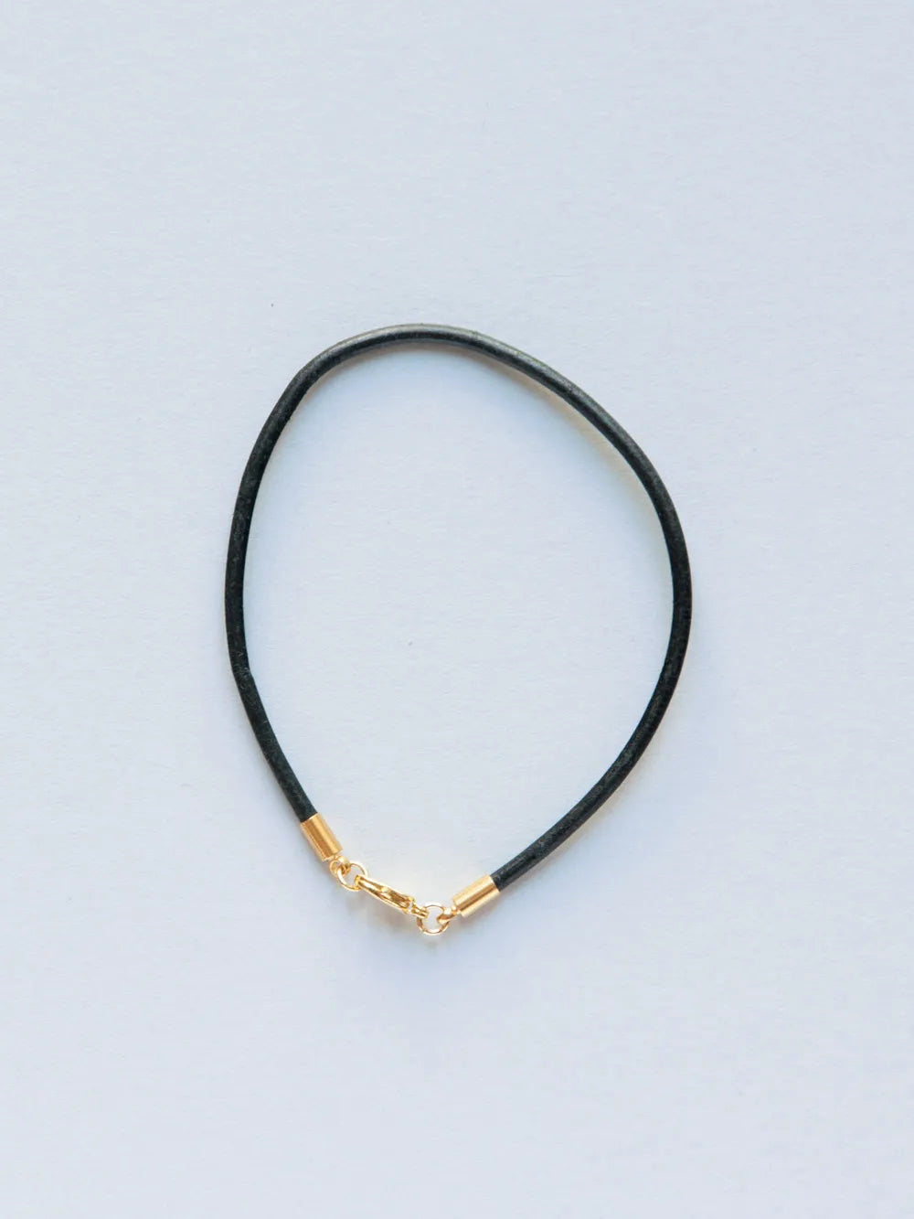Armband aus schmaler schwarzer Lederkordel mit goldenem Verschluss auf weissem Hintergrund