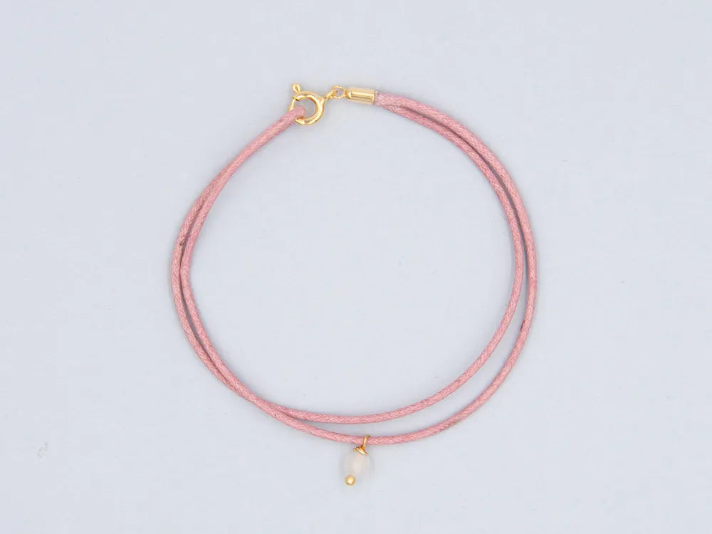 Armband altrosa aus gewachster Baumwollkordel mit runder Steinperle Rosenquarz und goldenem Verschluss vor weissem Hintergrund
