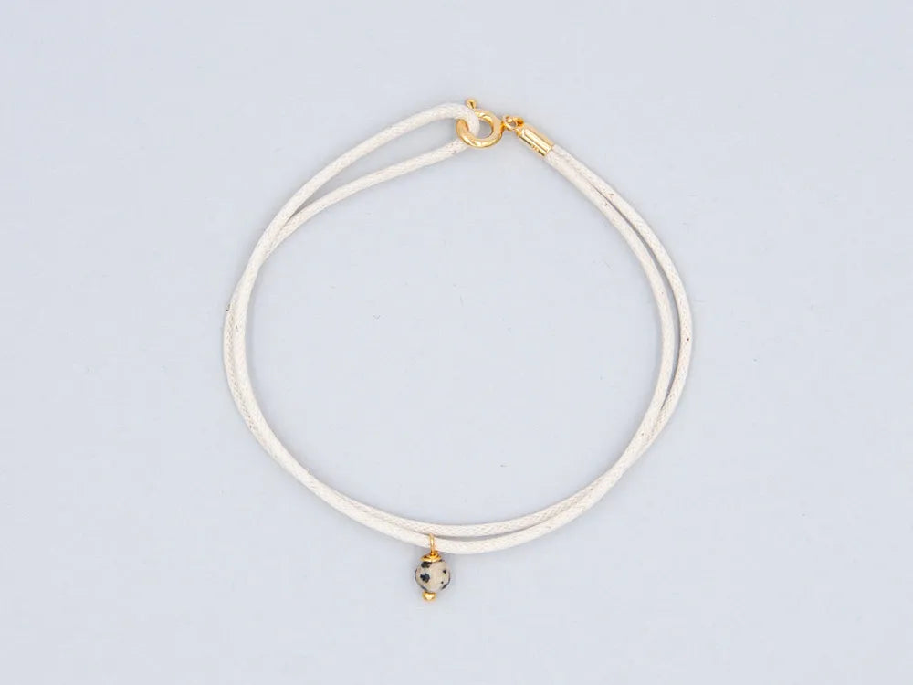 Armband cremefarben aus gewachster Baumwollkordel mit runder Steinperle Dalmatinerjaspis und goldenem Verschluss vor weissem Hintergrund