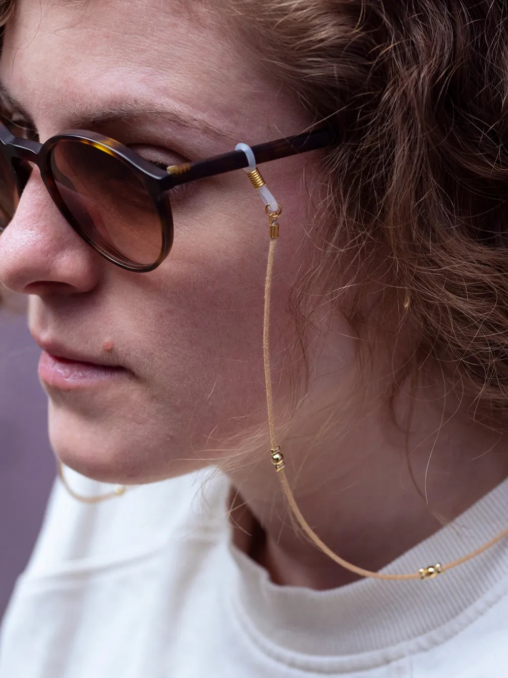 Detailansicht eines Gesichts, seitlich mit Sonnenbrille und Brillenband Baumwolle mit goldenen Perlen