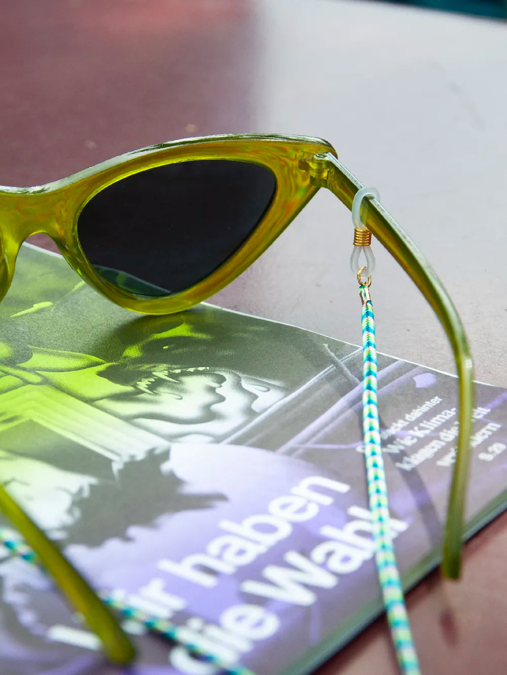 Grüne Sonnenbrille mit grün-blauem Brillenband auf Magazin