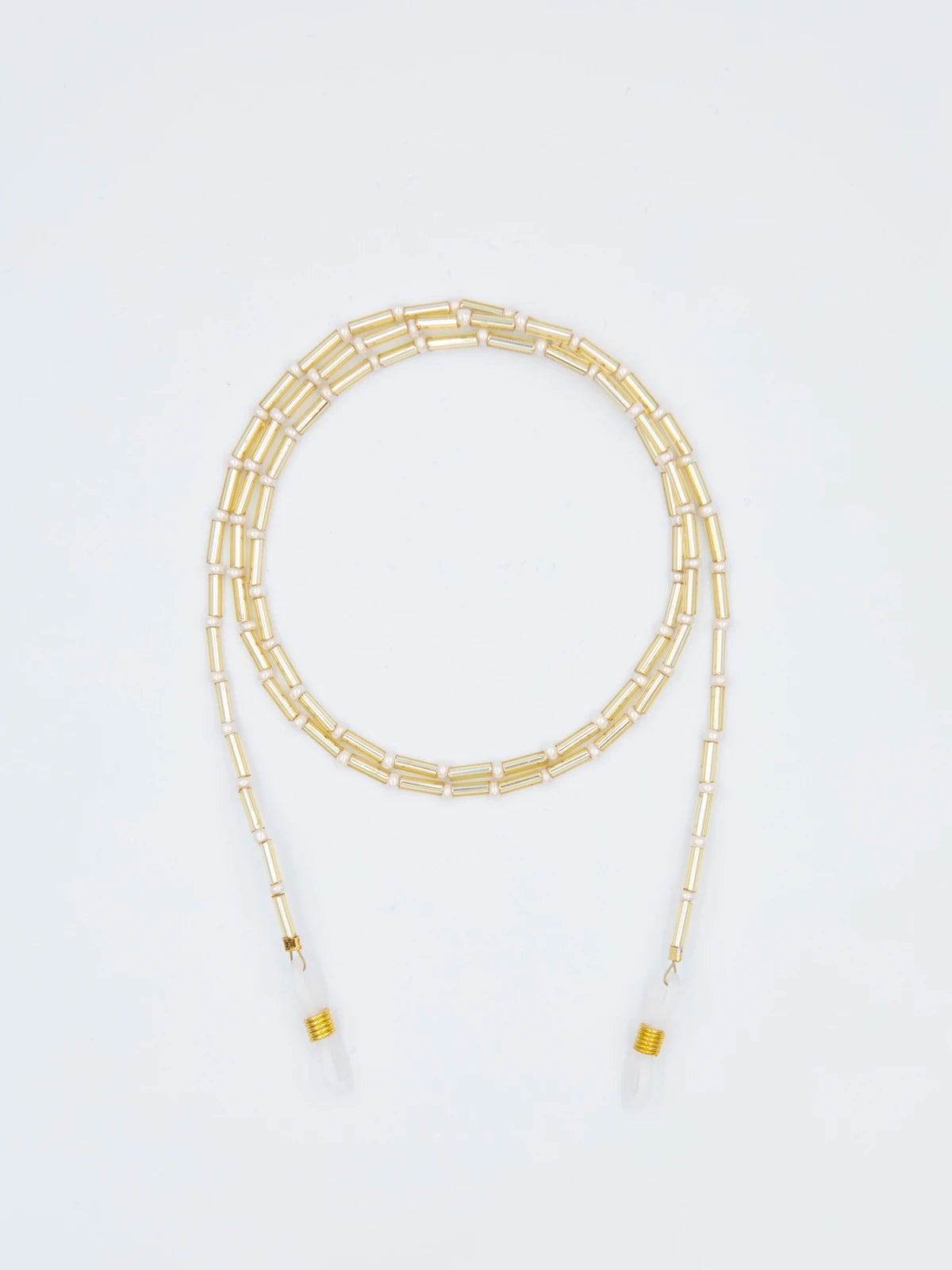 Brillenband aus goldenen Tube Perlen und crème farbenen feinen Glasperlen mit transparenten Brillengummis auf hellgrauem Hintergrund