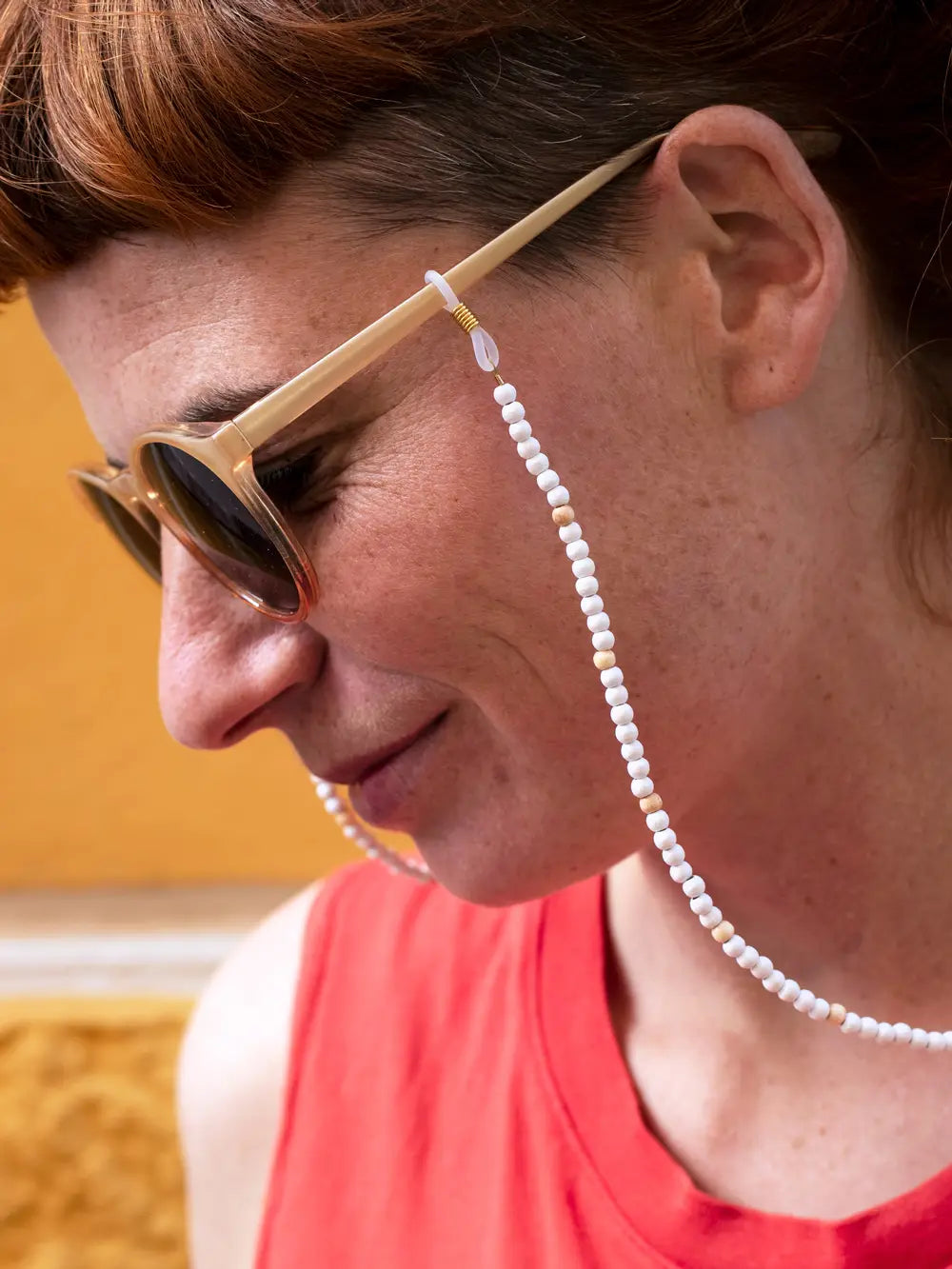 Seitenansicht eines Gesichts mit Sonnenbrille mit einem Brillenband aus weissen und naturfarbenen Holzperlen