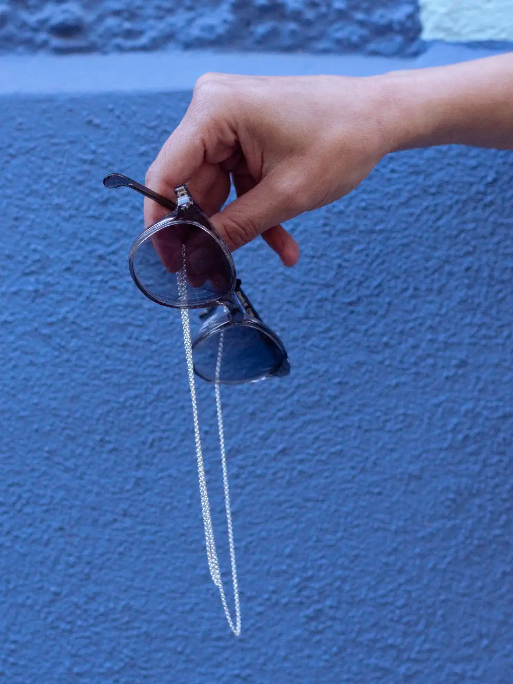 Hand hält Sonnebrille mit silbernem Brillenband aus feiner Kette