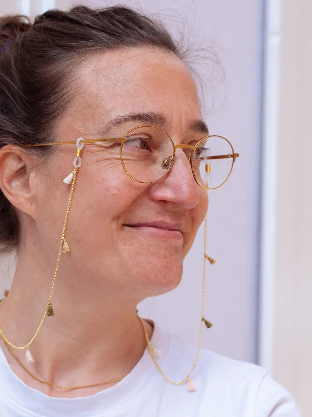 Person trägt goldene Brille mit goldenem Brillenband mit creme, beige und oliv Quasten vor weissem Hintergrund