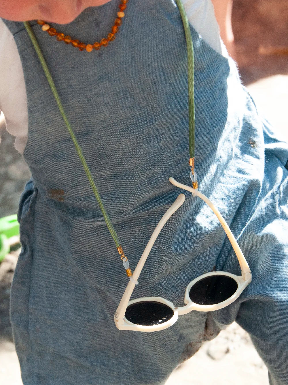 Frontansicht eines Kinderoberkörpers mit hellgrünem Brillenband und weisser Sonnenbrille