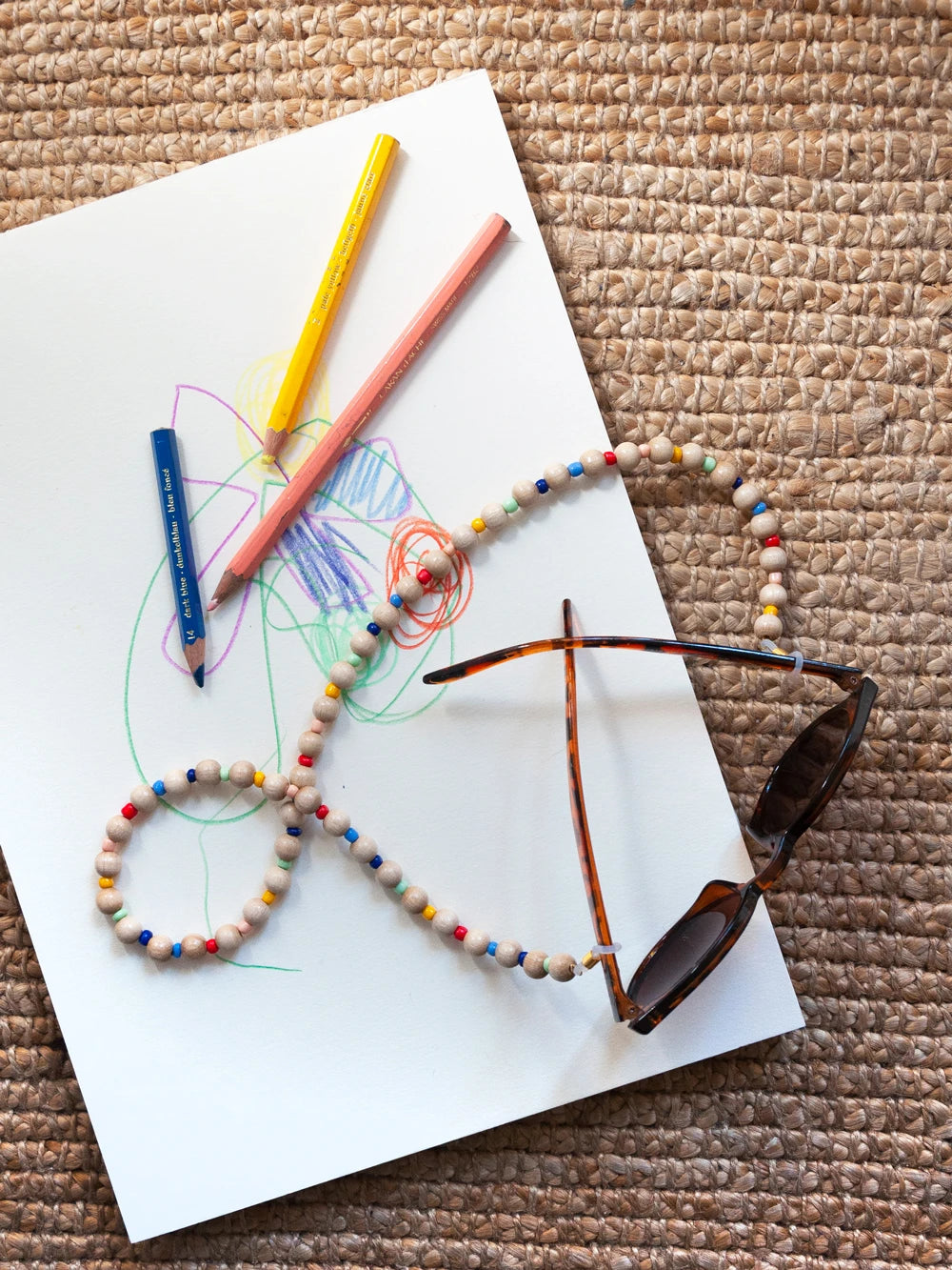 Obersicht einer Sonnenbrille mit Brillenband aus Holz- und Kunststoffperlen, auf Kinderzeichnung