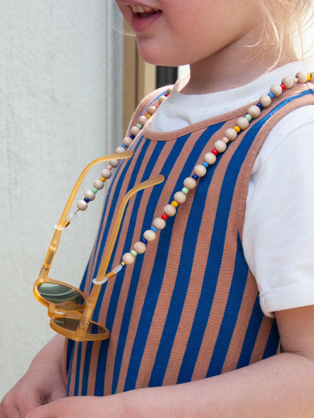 Seitenansicht eines Kinderoberkörpers, Sonnenbrille an Brillenband um den Hals gehängt.
