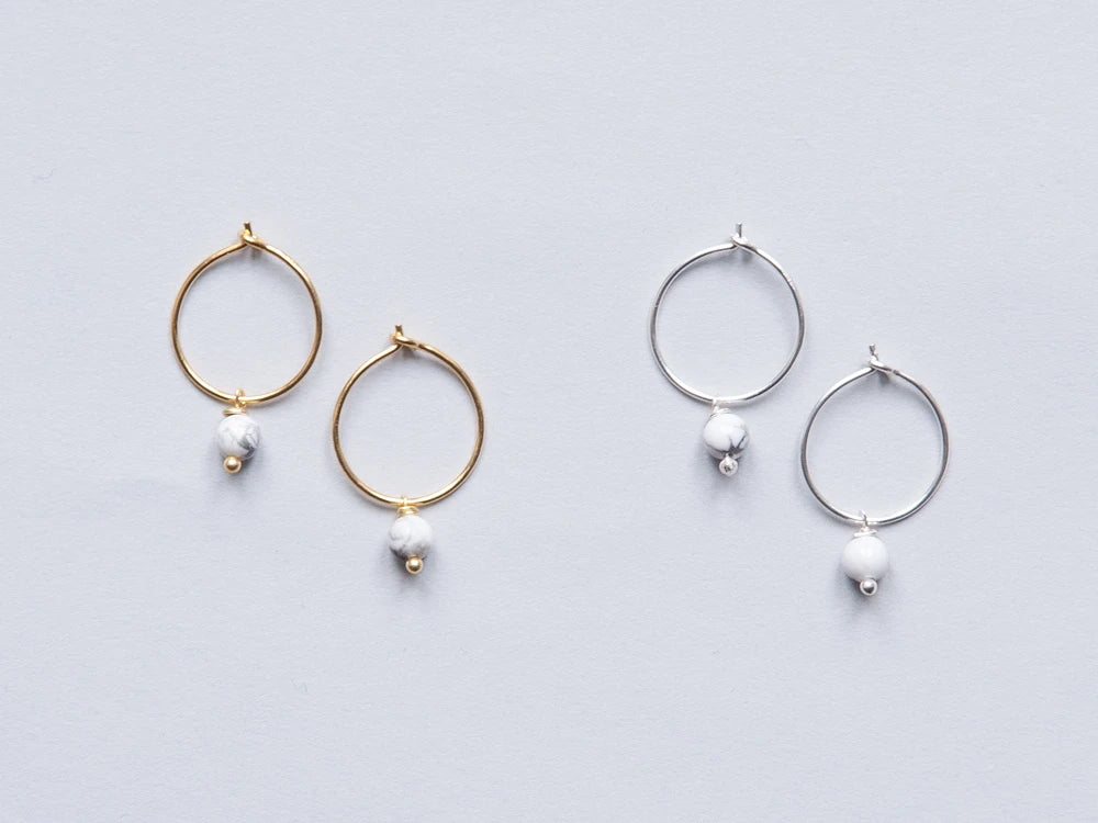 Zwei Paar Creolen in gold und silber mit je einer weiss-grauen runden Steinperlen auf grauem Hintergrund
