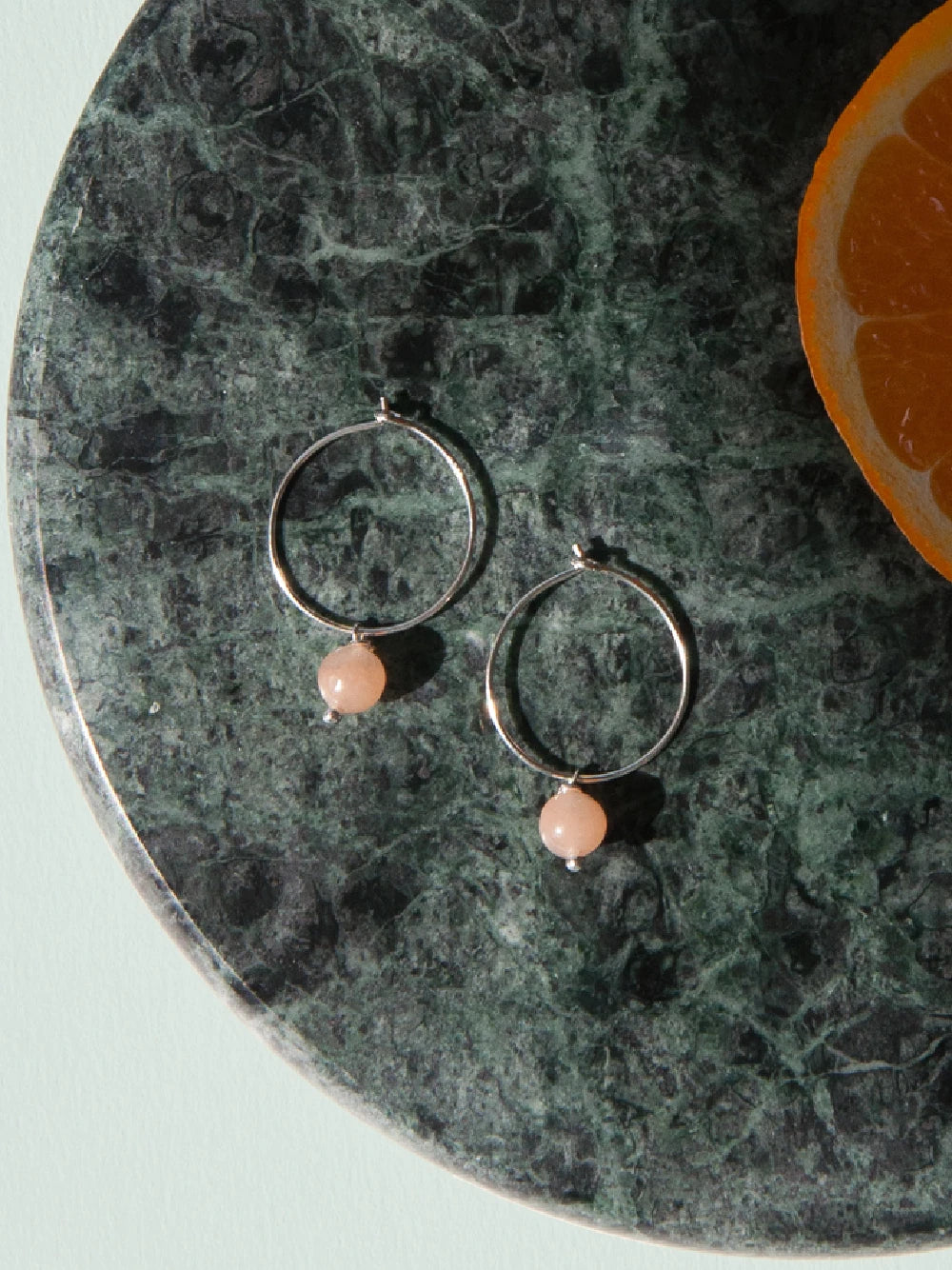 Silberne Creolen mit je einem runden Rosenquarzstein liegen auf einer runden Marmorplatte