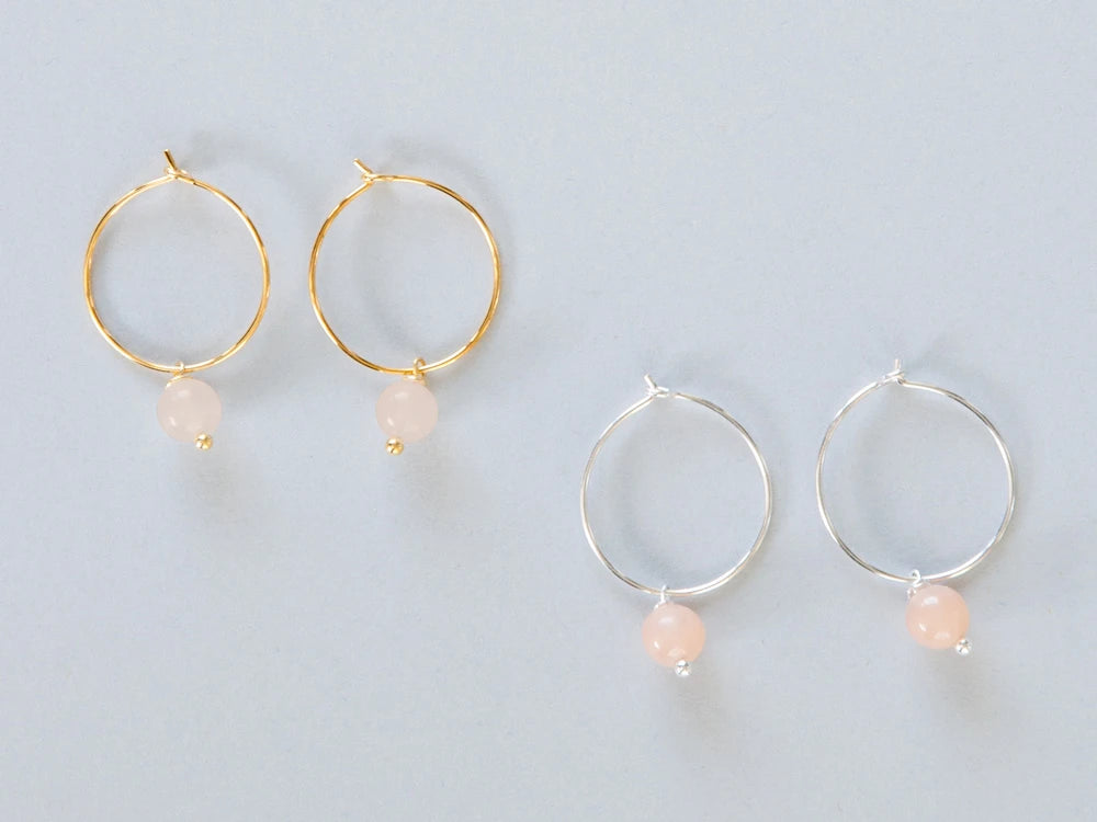 Zwei paar Creolen, einmal in silber und einmal in gold mit je einem runden Steinanhänger in rosa auf weissem Hintergrund