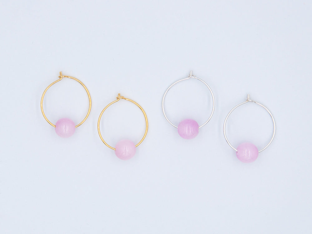 Zwei paar Creolen, einmal in silber und einmal in gold mit je einer runden Steinperle aus rosa Jade auf weissem Hintergrund
