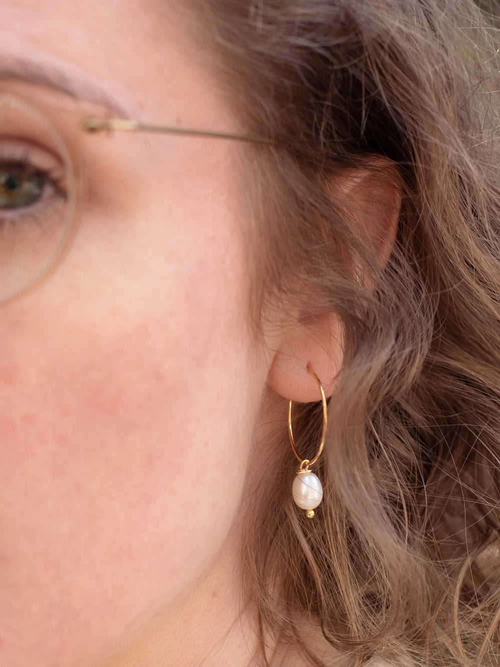 Detailansicht eines Ohrs mit goldenem Ohrring mit Perlanhänger