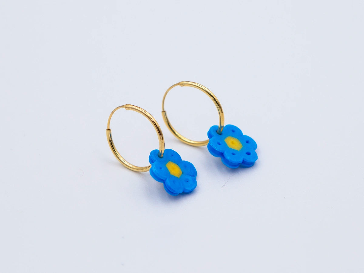 Zwei goldene Creolen mit Blume aus blauen Bügelperlen als Anhänger auf weissem Hintergrund