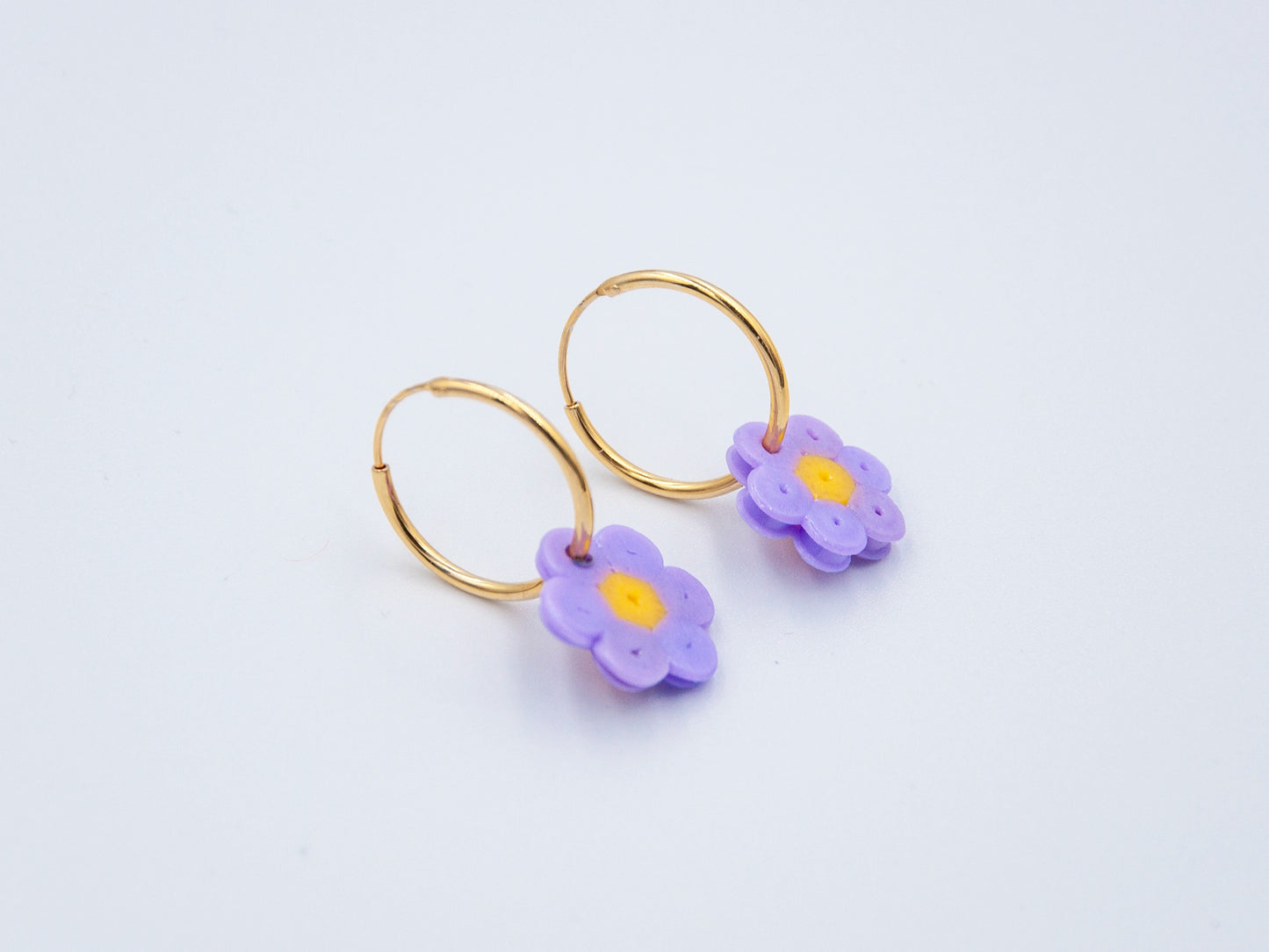 Zwei goldene Creolen mit Blume aus lila Bügelperlen als Anhänger auf weissem Hintergrund