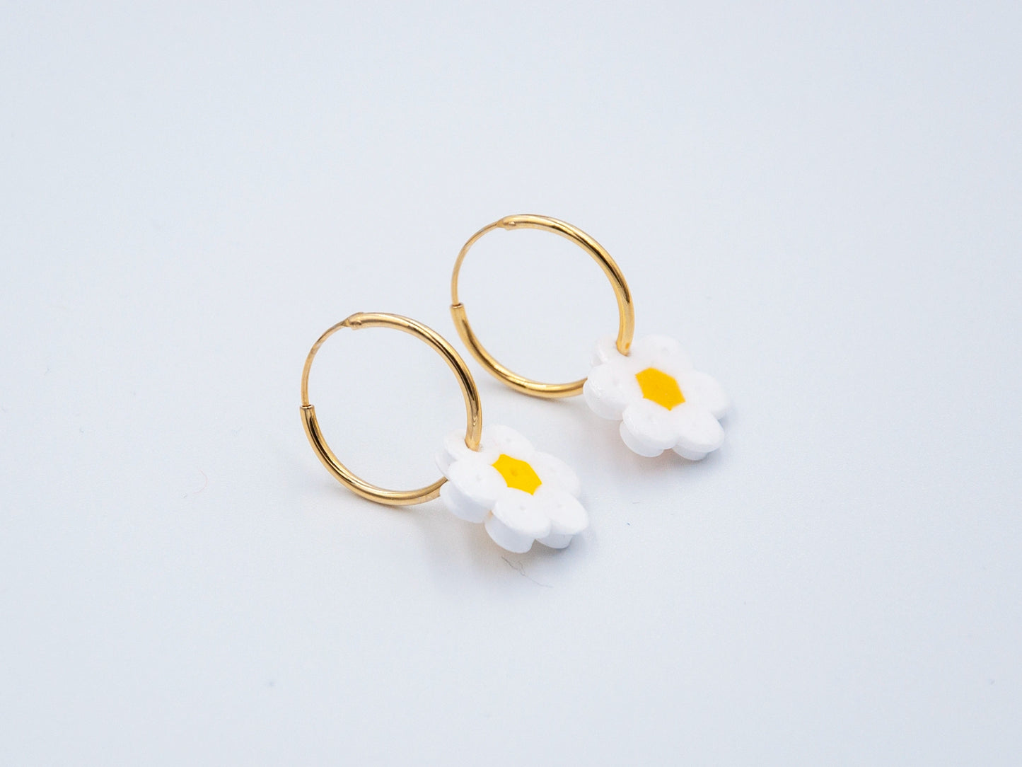 Zwei goldene Creolen mit Blume aus weissen Bügelperlen als Anhänger auf weissem Hintergrund
