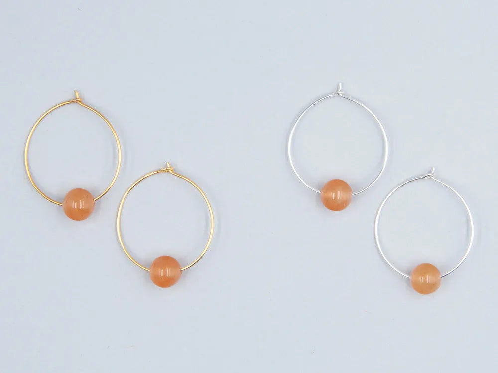 Zwei paar Creolen, einmal in silber und einmal in gold mit je einer runden Steinperle in orange auf weissem Hintergrund