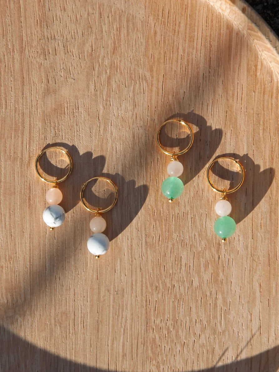 Zwei Paar Ohrringe auf Holz Hintergrund. Goldene kleine Ringe mit je zwei Steinperlen als Anhänger übereinander