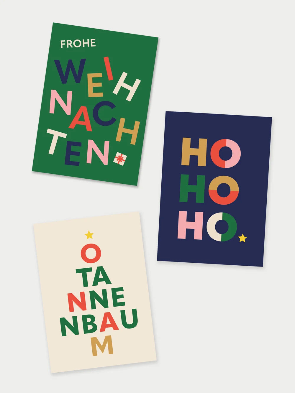 Drei Postkarten, eine Grün mit farbigem Schriftzug Frohe Weihnachten, eine dunkelblau mit Schriftzug HOHOHO, eine creme mit Schriftzug O Tannenbaum