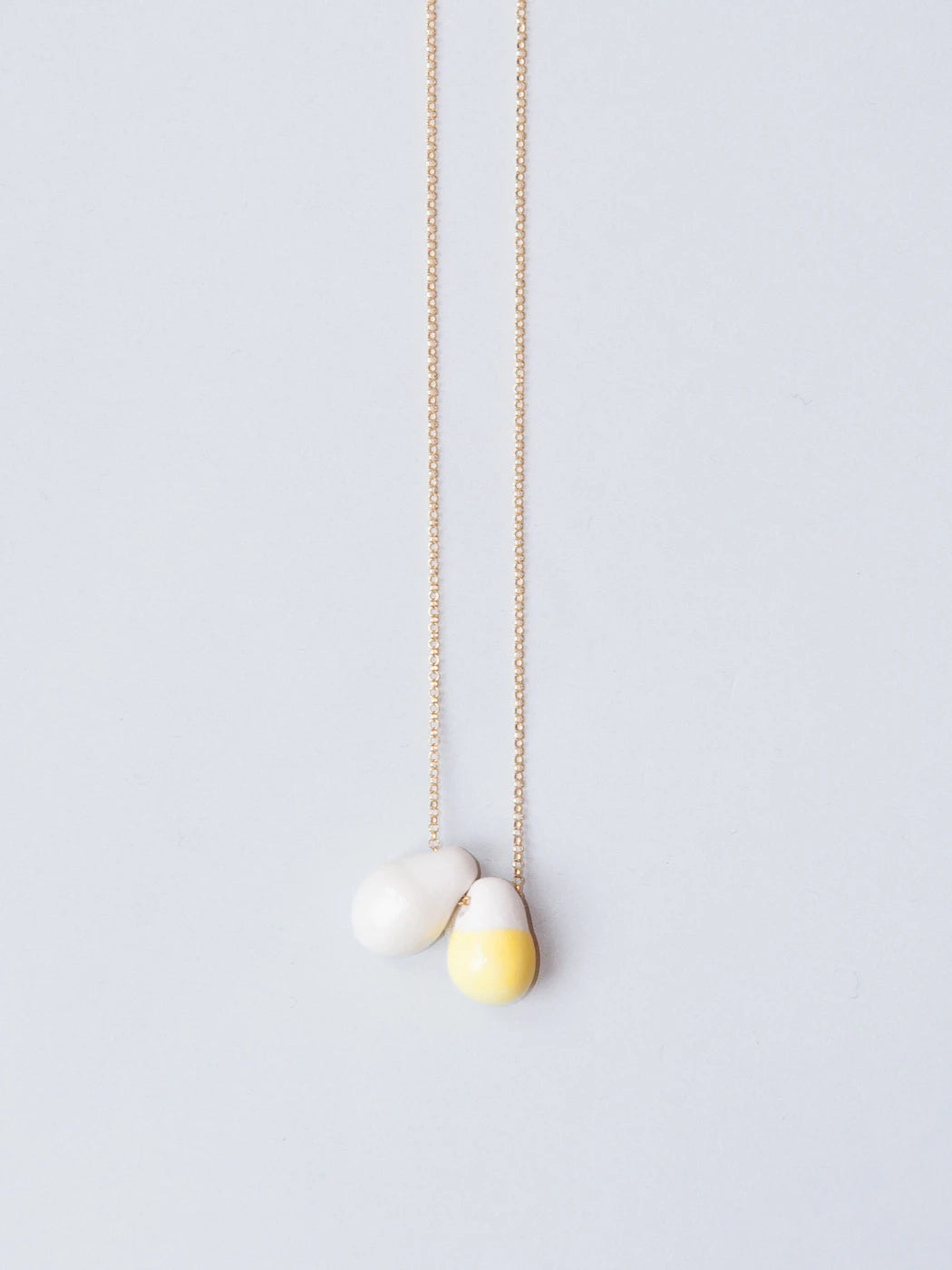 Goldene feine Kette mit zwei tropfenförmigen Porzellananhängern weiss und gelb auf weissem Hintergrund