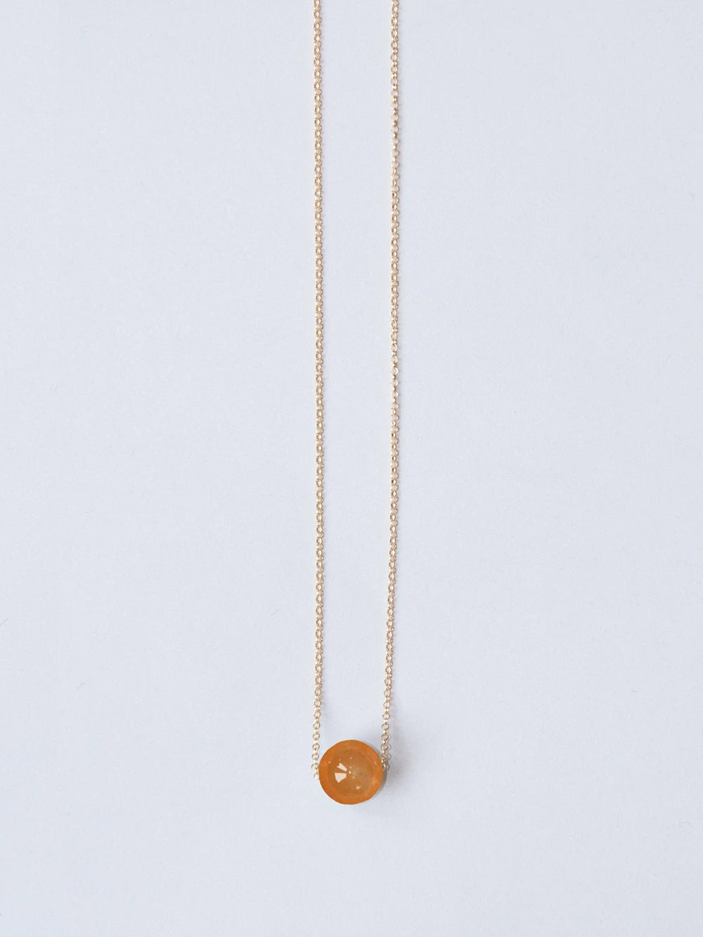 Goldene feine Kette mit Steinperle lachs auf weissem Hintergrund
