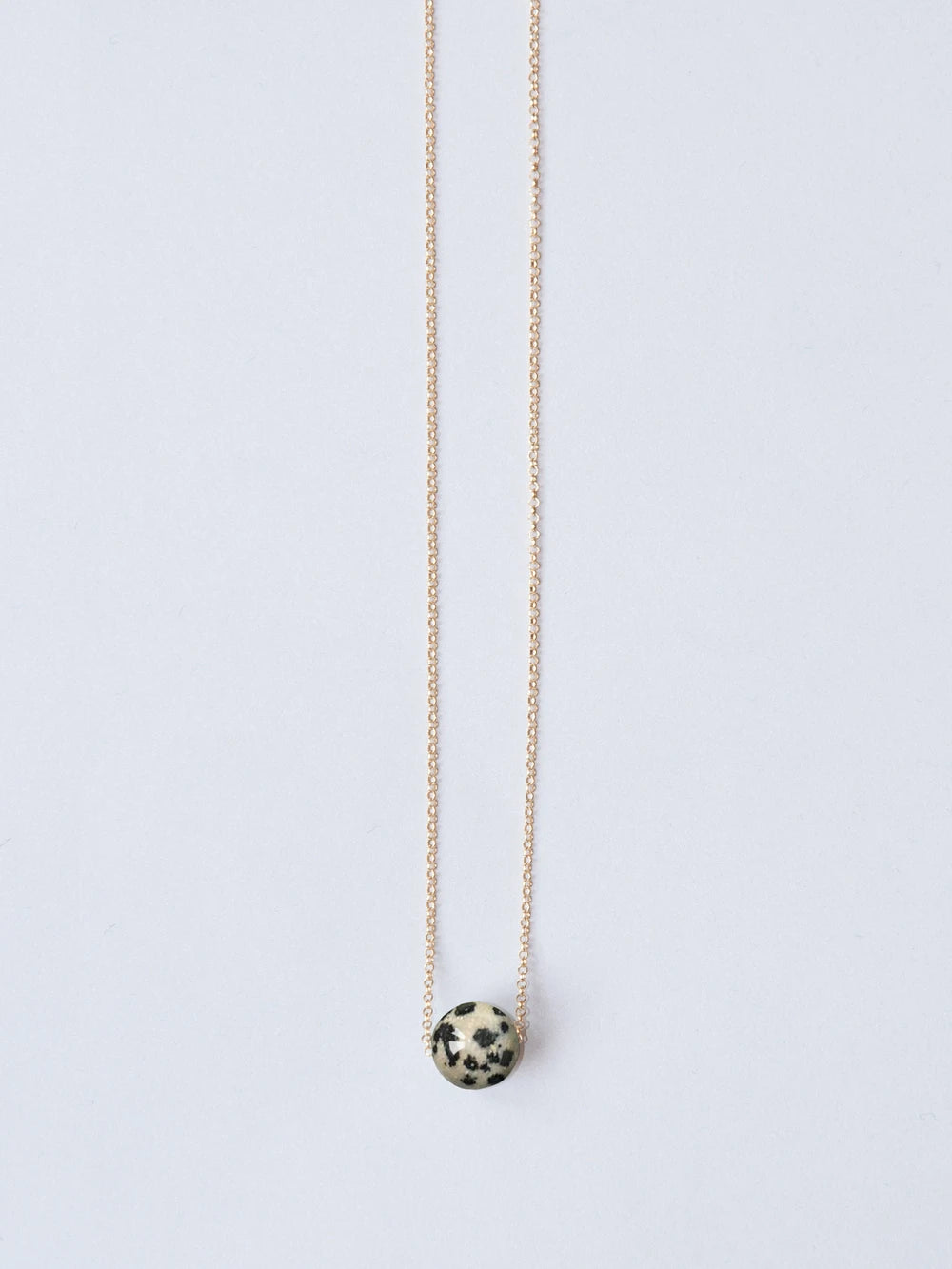 Goldene feine Kette mit Steinperle beige mit schwarzen Punkten auf weissem Hintergrund