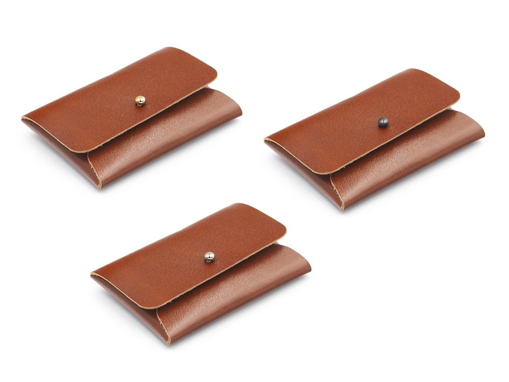drei braune Kartenportemonnaies aus Leder mit Kopfnieten als Verschlüssen auf weissem Untergrund
