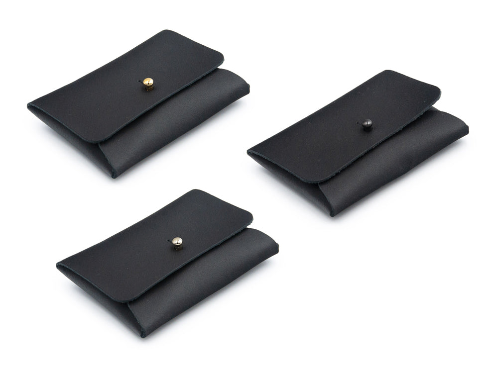 drei schwarze Kartenportemonnaies aus Leder mit Kopfnieten als Verschlüssen auf weissem Untergrund