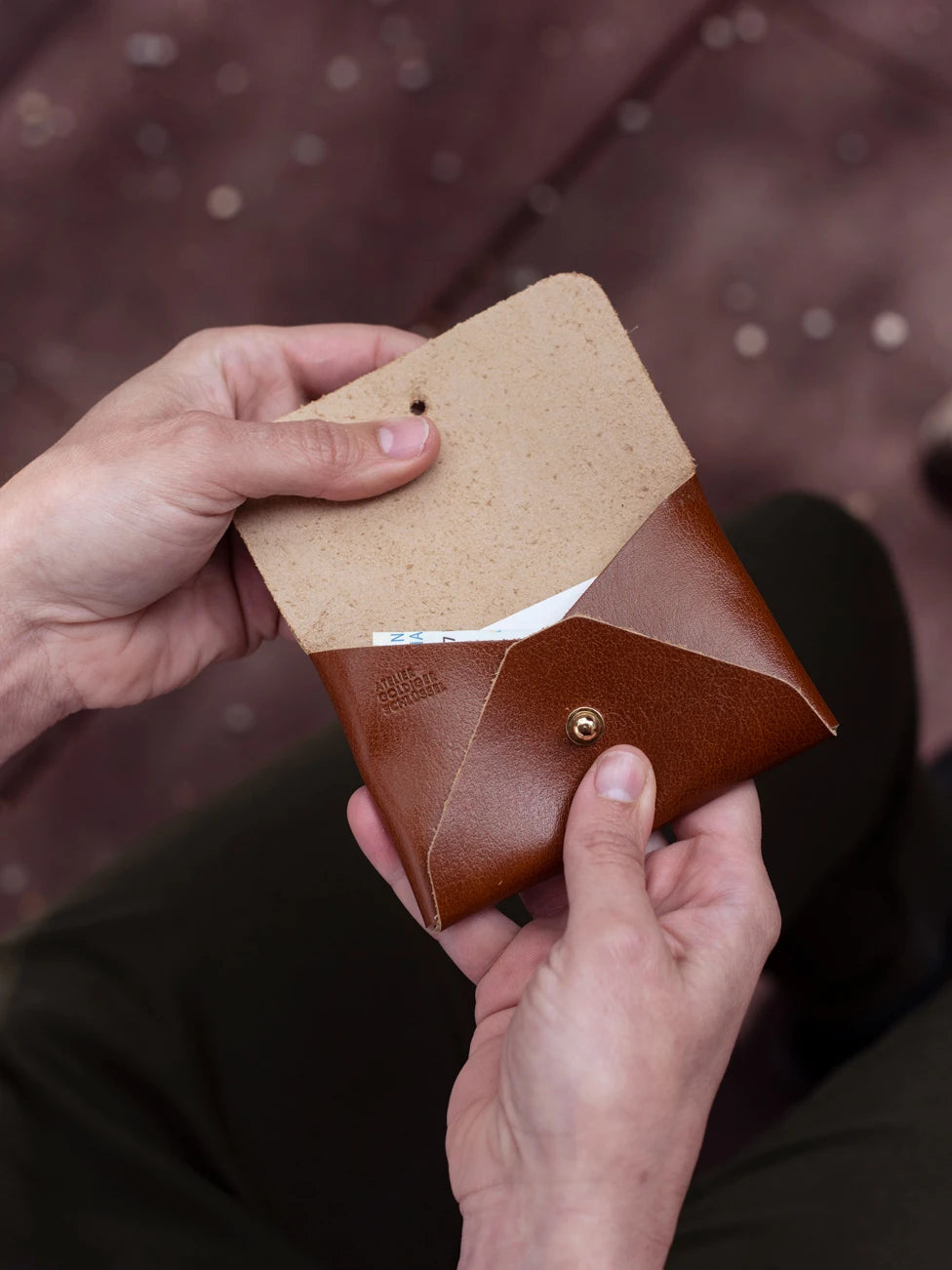 Zwei Hände halten ein Kartenportemonnaie aus braunem Leder mit der Prägung Atelier Goldiger Schlüssel