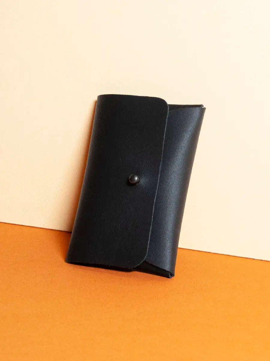 Kartenportemonnaie aus schwarzem Leder mit schwarzer Kopfniete als Verschluss auf orange-gelbem Hintergrund