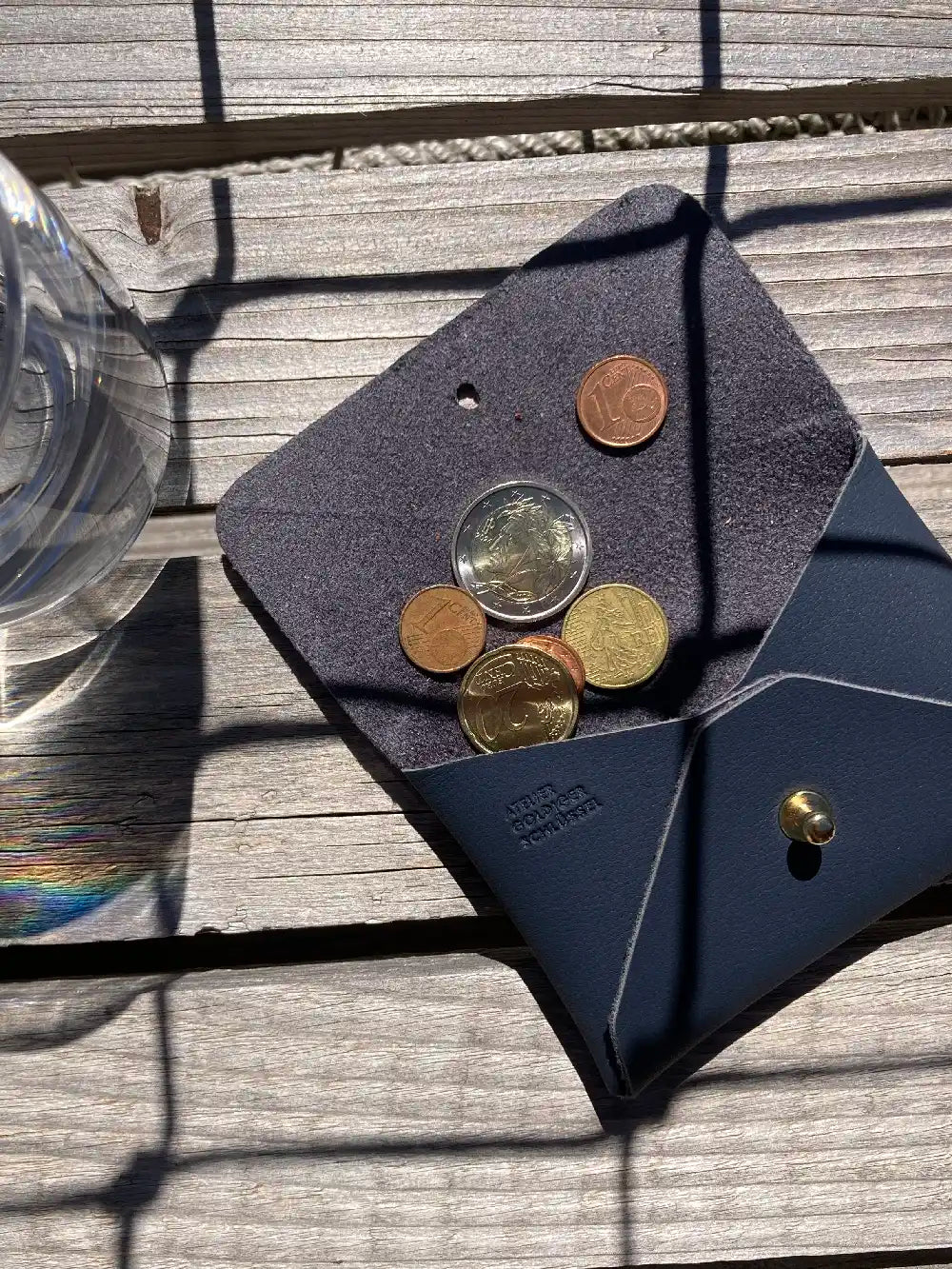 geöffnetes dunkelblaues Kartenportemonnaie mit Euromünzen liegt auf holzigem Untergrund