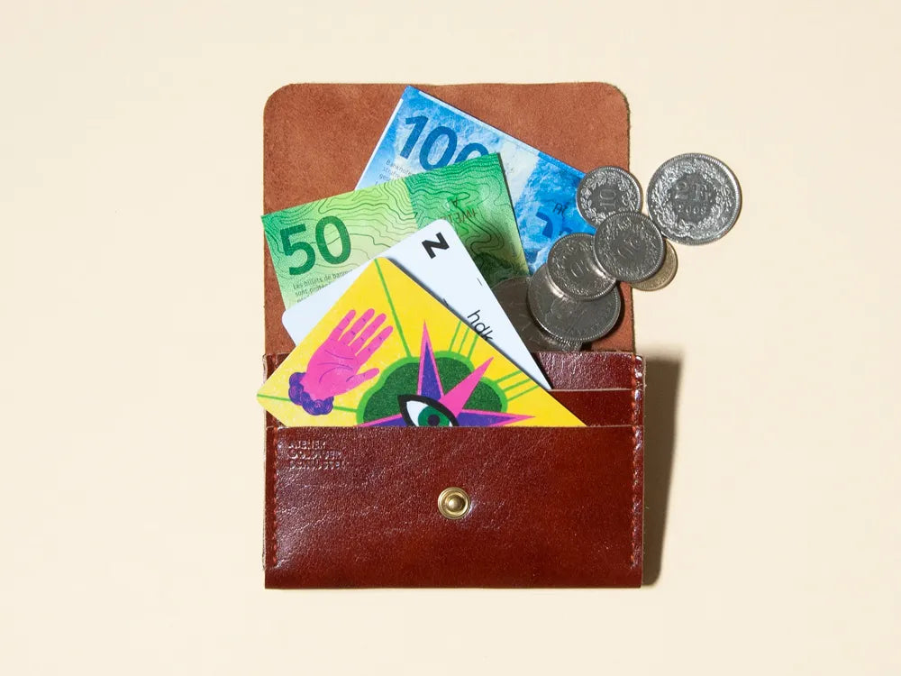 Ein rotbraunes Portemonnaie liegt offen da und ist mit Karten, Noten und Münz gefüllt