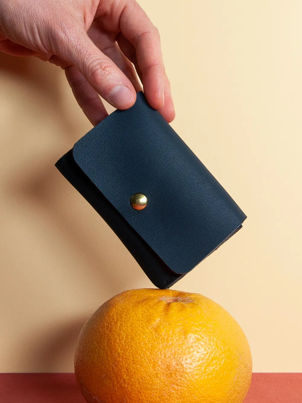 Hand hält von oben dunkelblaues Portemonnaie aus veganem Leder. Unten liegt eine Grapefruit.
