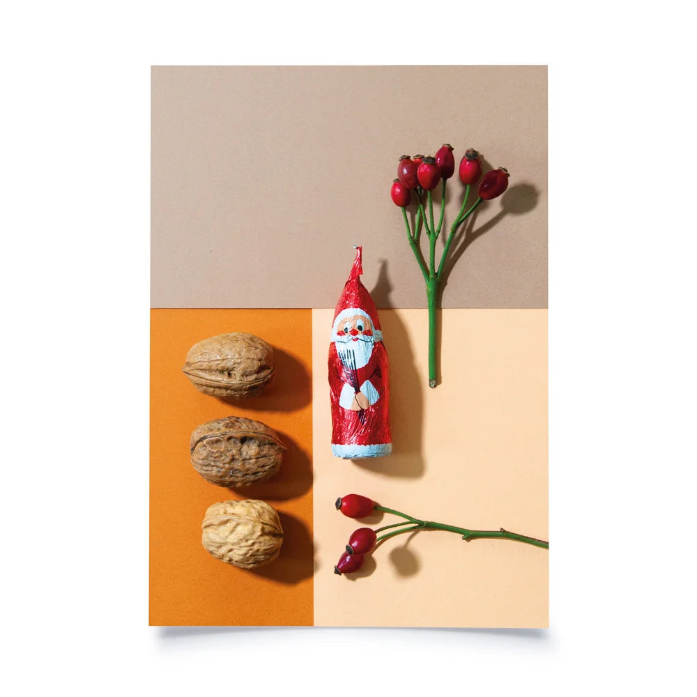 Postkarte mit Farbflächen in beige, creme und orange als Hintergrund, davor 3 Walnüsse, ein Schokosamichlaus und 2 Hagebuttenzweige