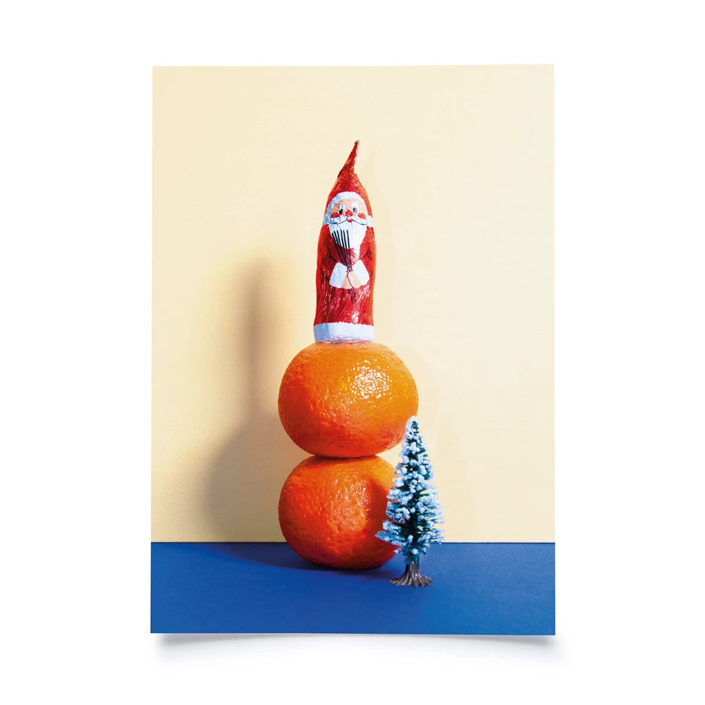 Postkarte mit Farbflächen in creme und blau als Hintergrund, davor 2 Mandarinen, darauf ein Schokosamichlaus und daneben eine Plastiktanne