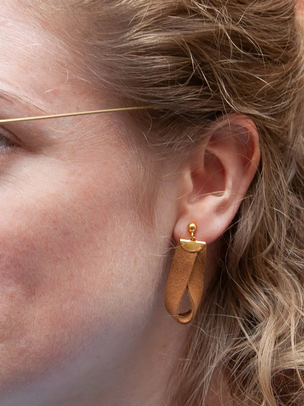 Detailansicht eines Ohrs mit Ohrhängern aus braunem Leder und goldenen Metallteilen