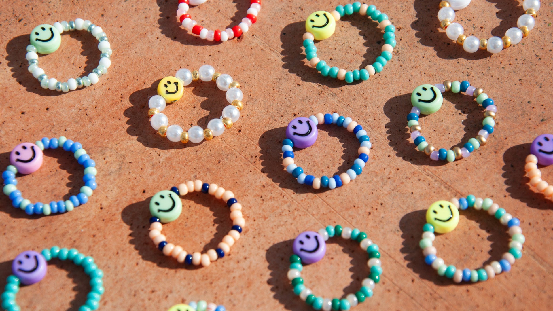 Viele unterschiedliche bunte Ringe aus Glasperlen und Smiley auf terracotta farbenem Untergrund.