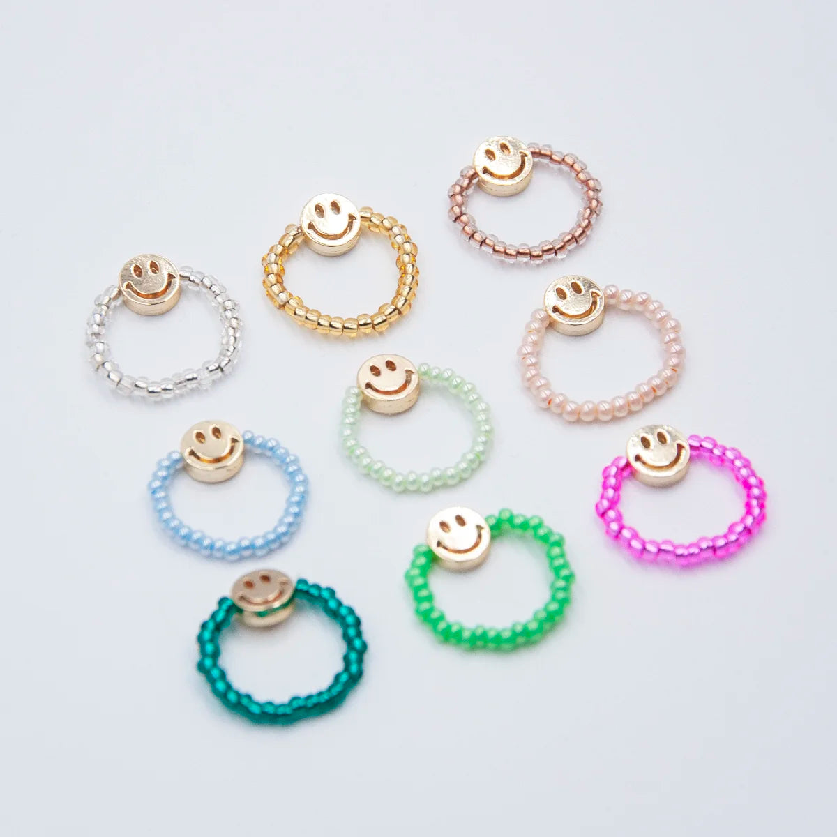9 unterschiedliche bunte Glaspelrlenringe mit je einer goldigen Smileyperle