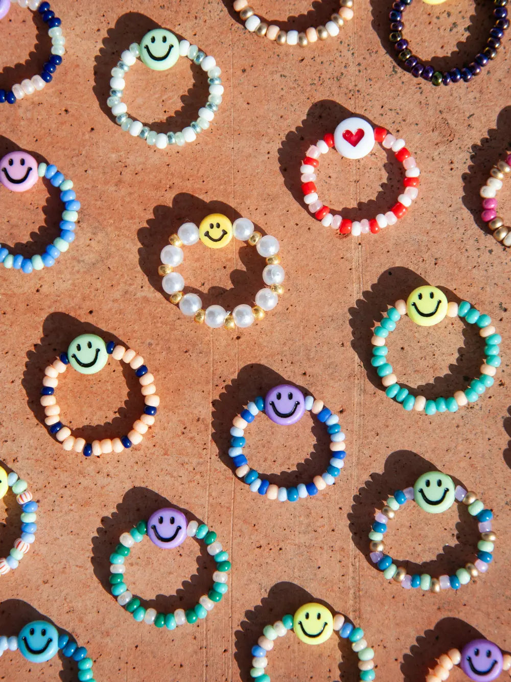Viele bunte Glasperlen Fingerringe mit je einer Smiley Perle auf terrakota Untergrund