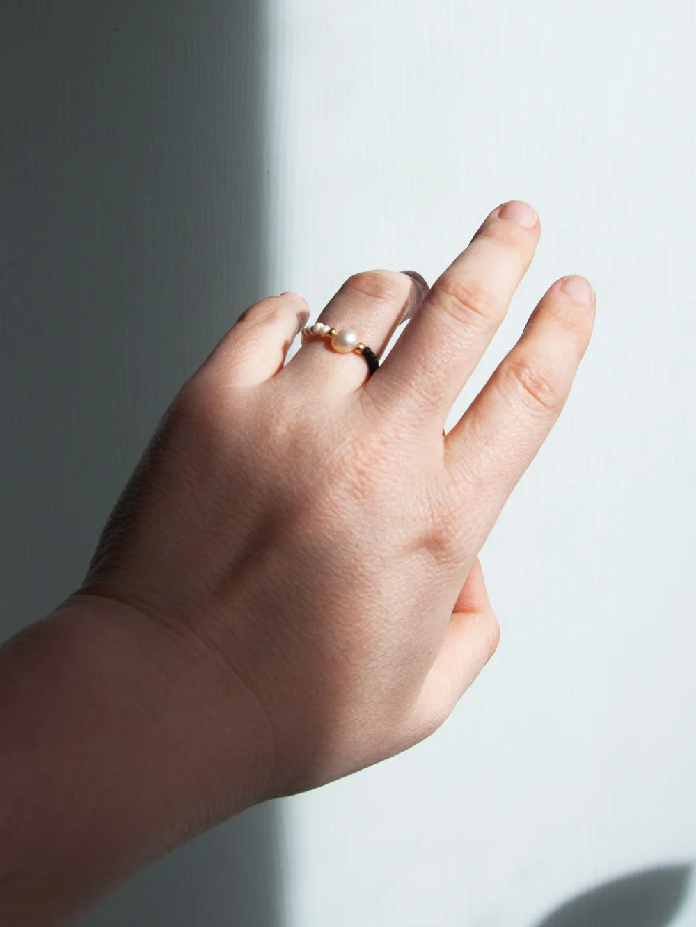 Hand im Sonnenlicht die einen Glasperlen Ring mit Süsswasserperle trägt