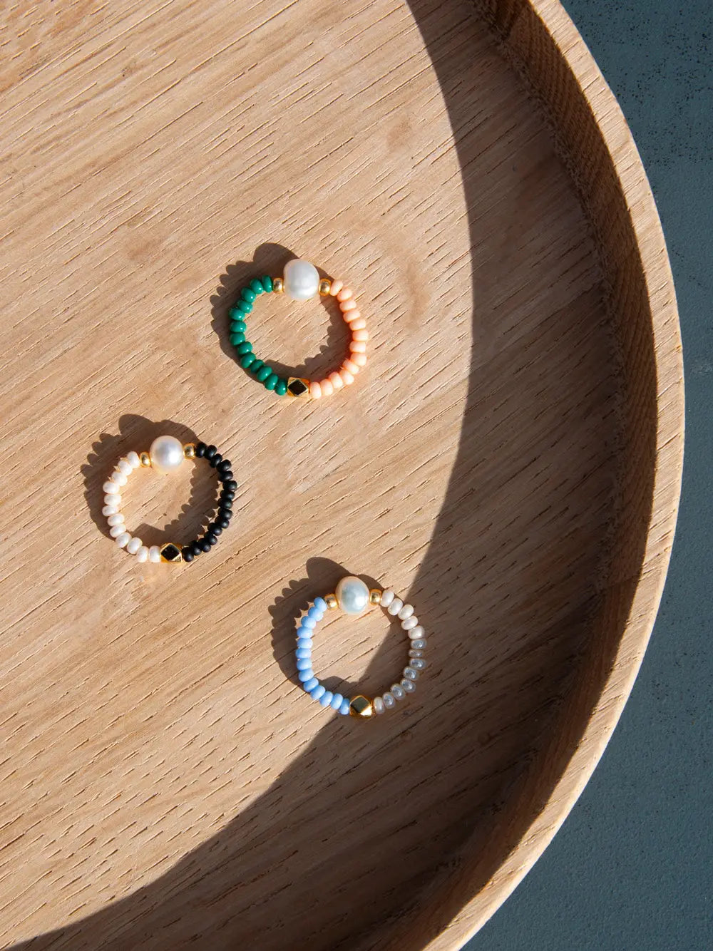 Drei Glasperlen Ringe mit je einer Süsswasserperle auf einem Holztablett