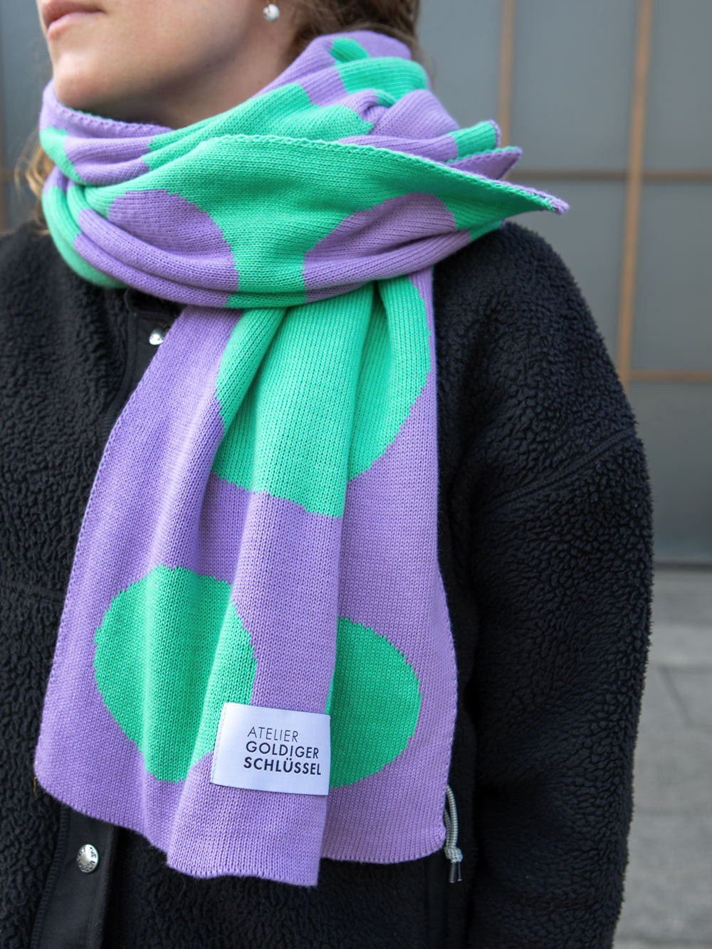 Frau mit schwarzer Teddy Jacke trägt lila mint gepunkteten Schal mit des Labels "Atelier Goldiger Schlüssel"
