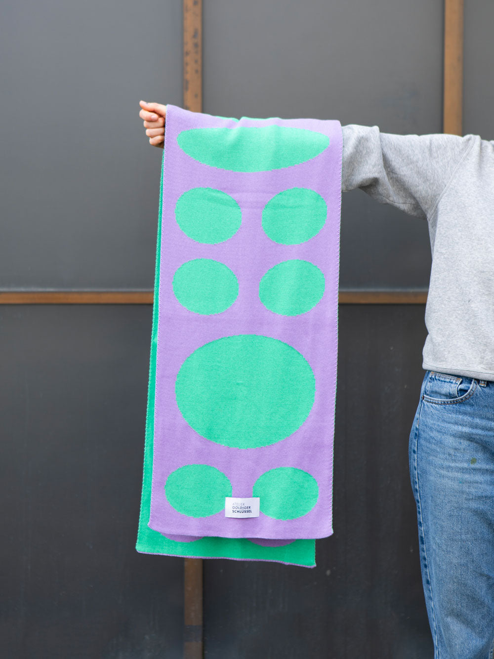 lila mint gepunkteter gestrickter Schal liegt über ausgestrecktem Arm
