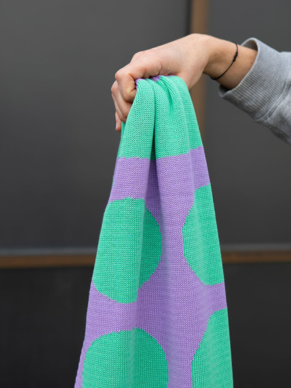 Hand hält von rechts einen mint lila gestrickten Schal ins Bild