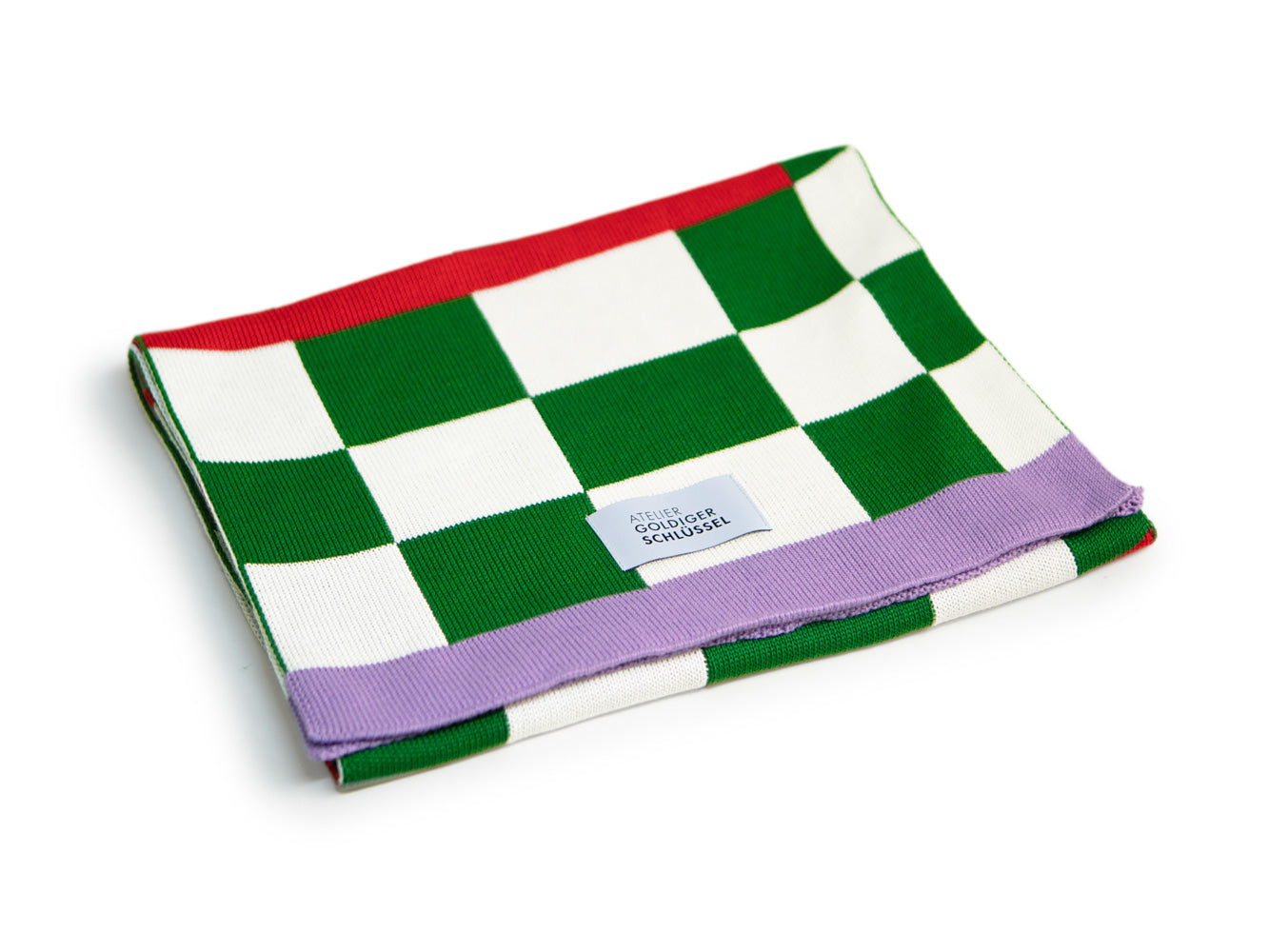 grün-weiss karierter Schal mit violettem Ende liegt gefaltet auf weissem Hintergrund.