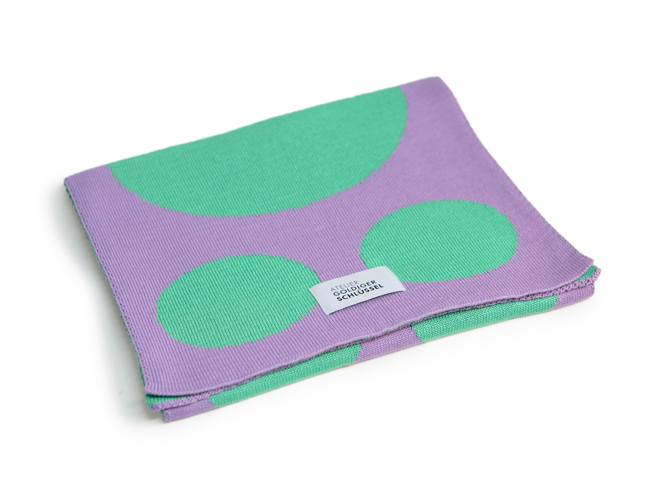 Mint lila gepunkteter Strickschal des Labels Atelier Goldiger Schlüssel liegt gefaltet auf weissem Hintergrund
