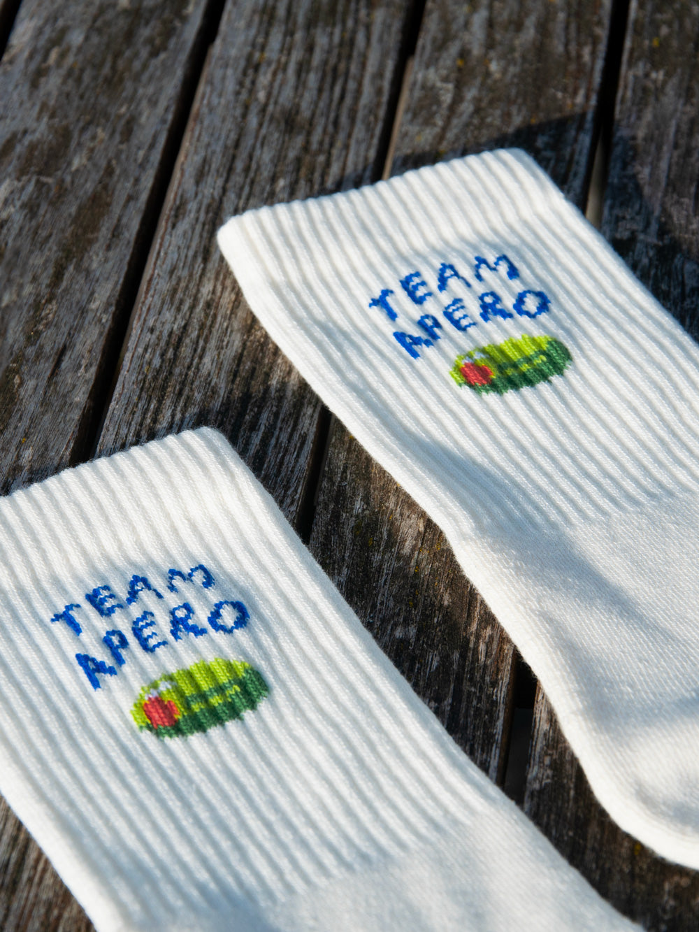 Eine Detailansicht vonden Bündchen zweier weisser Sportsocken mit dem eingestrickten Motiv Team Apéro und einer grünen Olive.