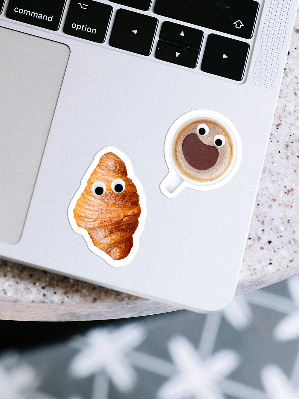 Detailansicht eines Macbooks auf dem zwei Sticker von einer Kaffetasse und einem Gipfeli mit Wackelaugen kleben.
